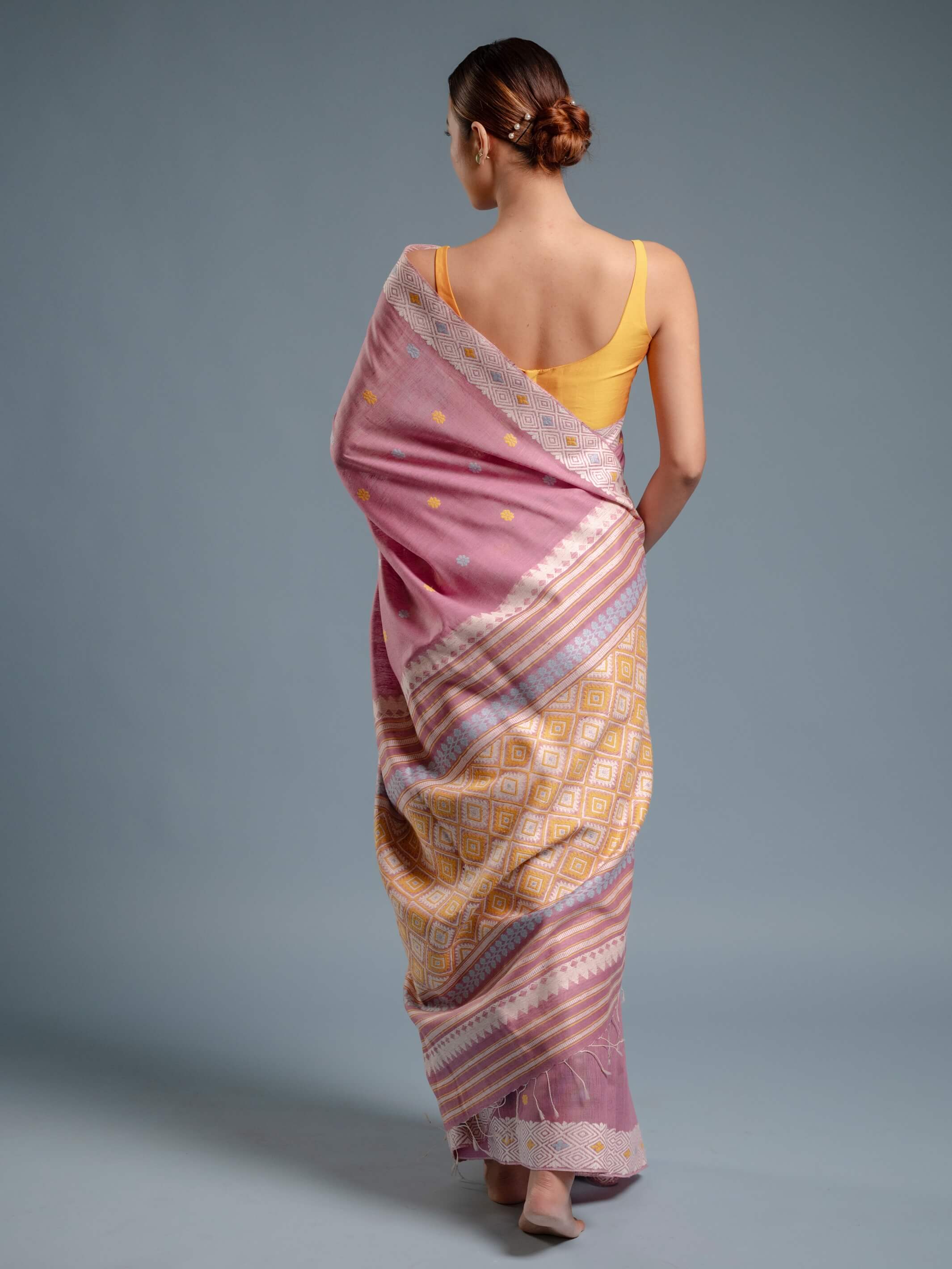 Woman wearing a lilac pink and yellow saree with a plain background