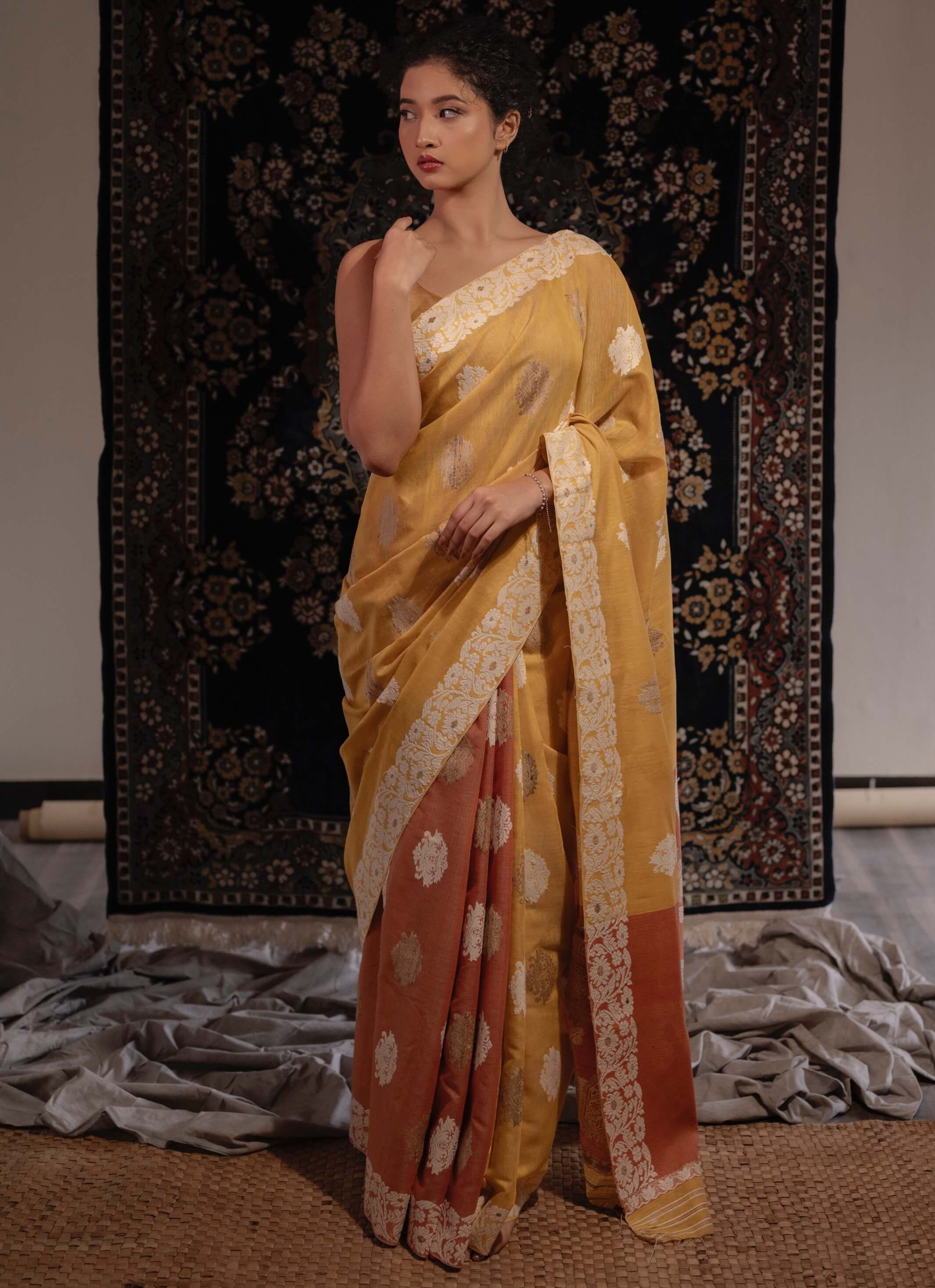 A model showcasing a naturally-dyed mustard yellow and lac rust orange silk saree with floral and paisley motifs and a woven floral border.