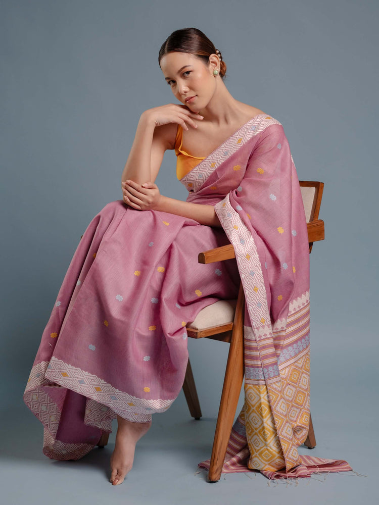 Woman sitting on a chair wearing a lilac pink saree with a yellow blouse against a gray background