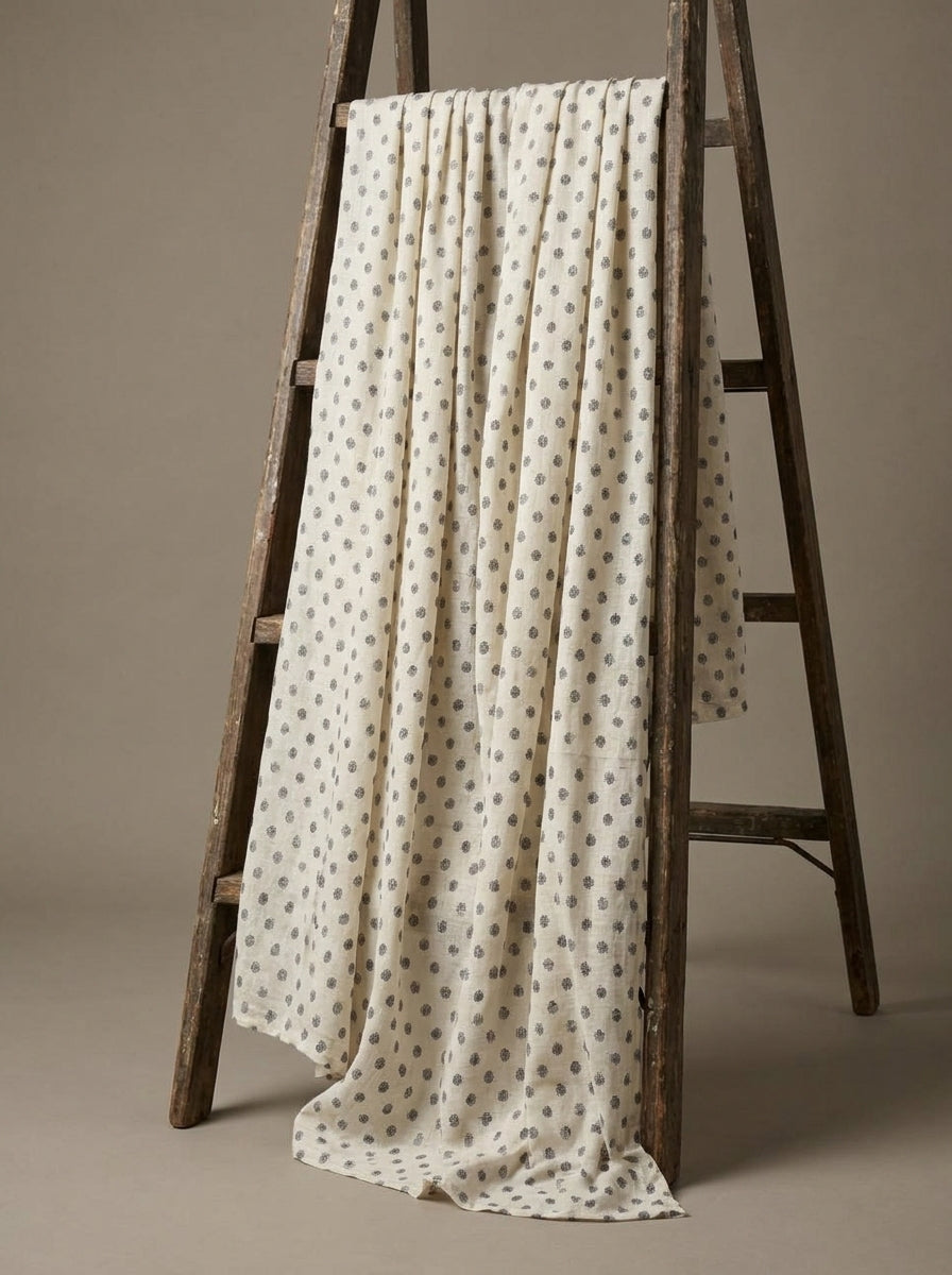 An off-white Eri silk fabric with a small gray geometric pattern draped over a rustic wooden A-frame ladder against a neutral beige background.