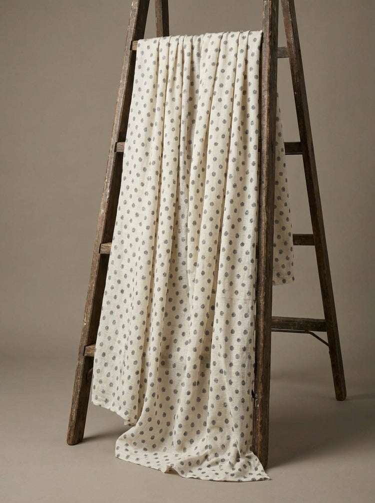 An off-white Eri silk fabric with a small gray geometric pattern draped over a rustic wooden A-frame ladder against a neutral beige background.