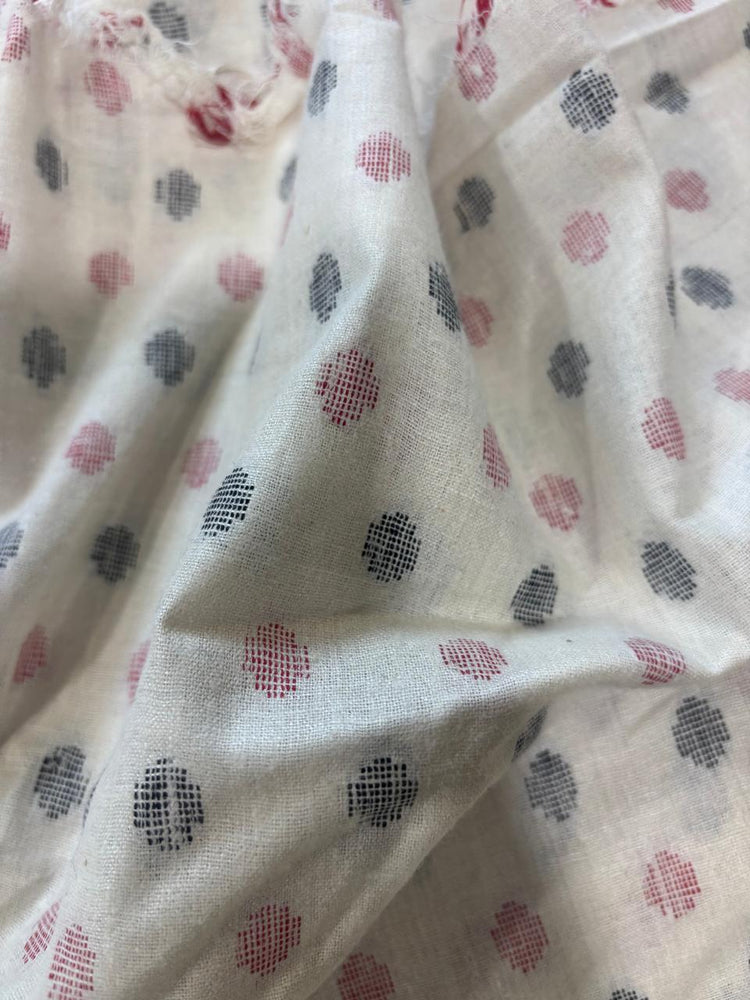 A close-up of off-white fabric with a scattered jamdani-style dot pattern in muted red and dark gray.