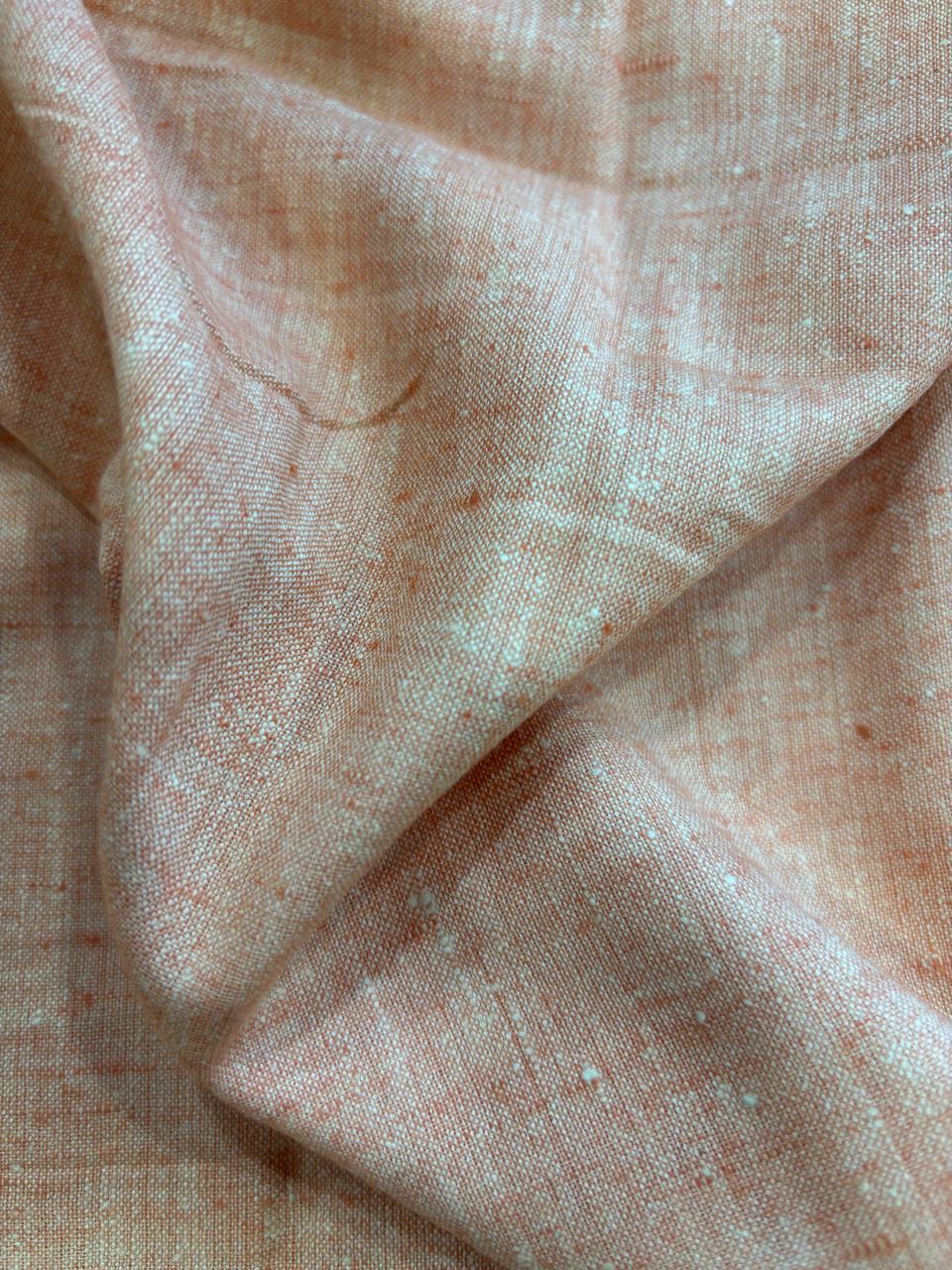 A close-up of draped peach-colored fabric with a subtle woven texture and tiny white flecks.