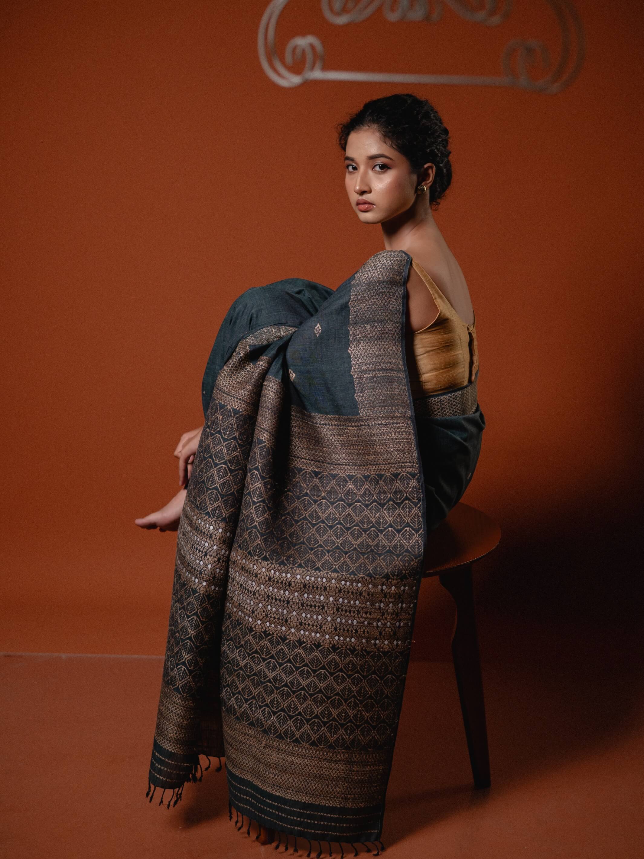 Woman draped in a traditional patterned fabric against an orange background