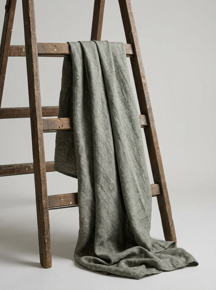 A textured, muted grey fabric draped over a rustic wooden ladder against a neutral light gray background.
