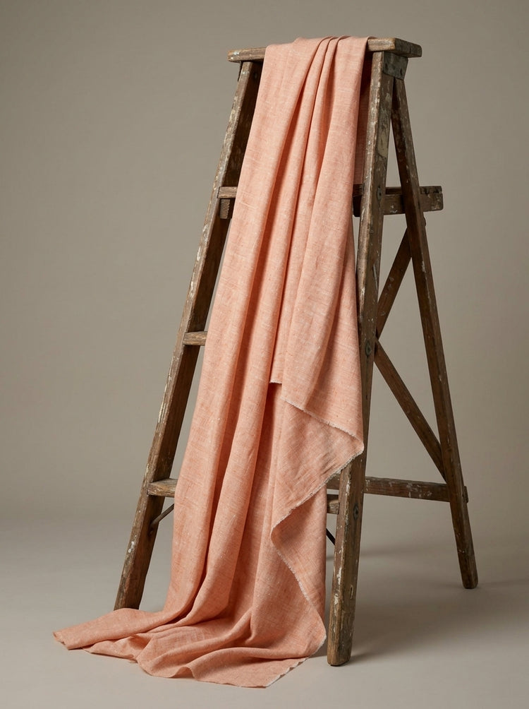 A peach-pink eri fabric draped over a rustic wooden A-frame ladder against a neutral taupe background.
