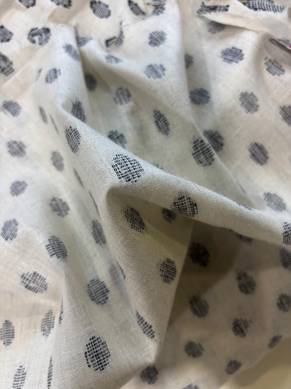 Close-up of a light cream or off-white fabric with a repeating dark gray woven dot pattern, shown in soft folds.