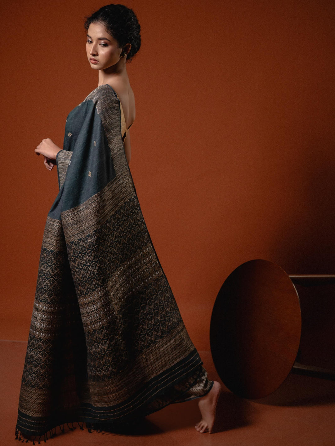 Woman wearing a woven teal blue saree against a brown background
